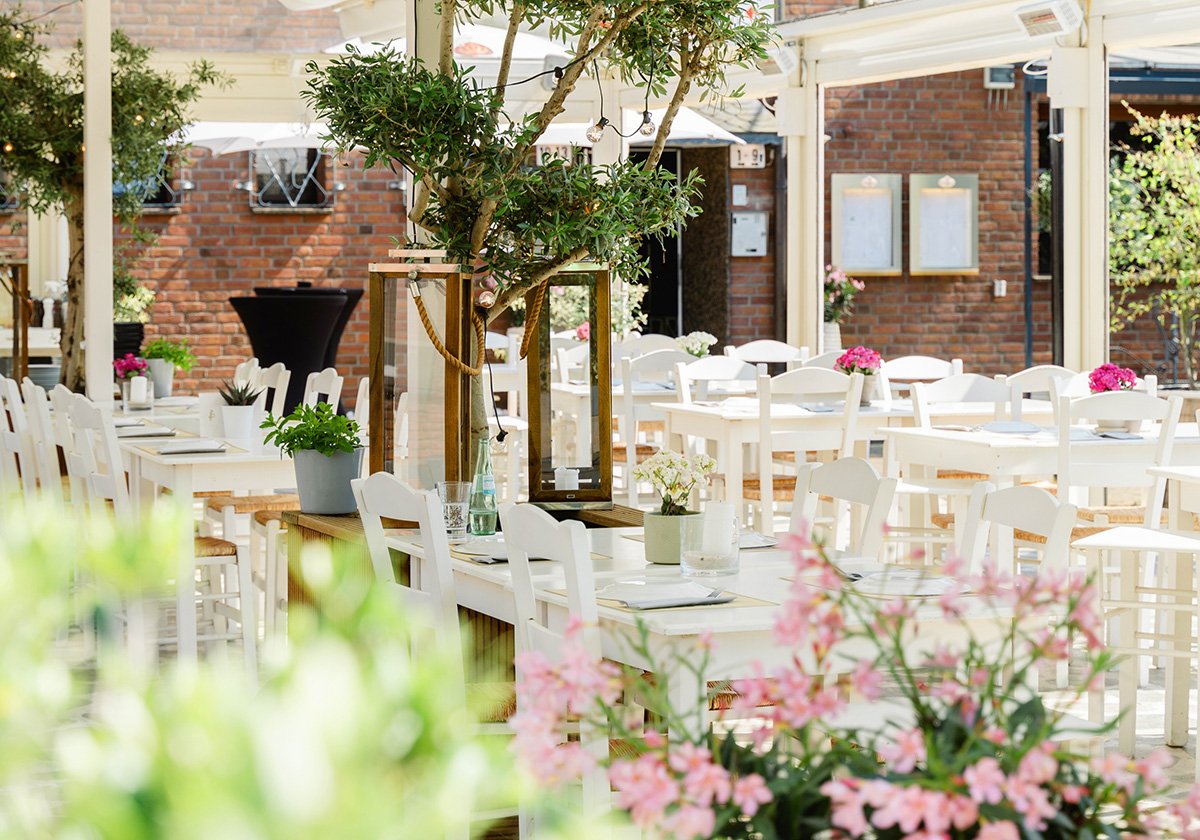 Überdachte Sommerterrasse mit Olivenbäumen und weißen Stühlen im Restaurant Omega Moers